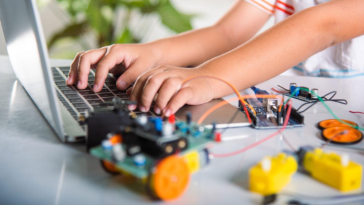 Young student hands on laptop while programming an Arduino board