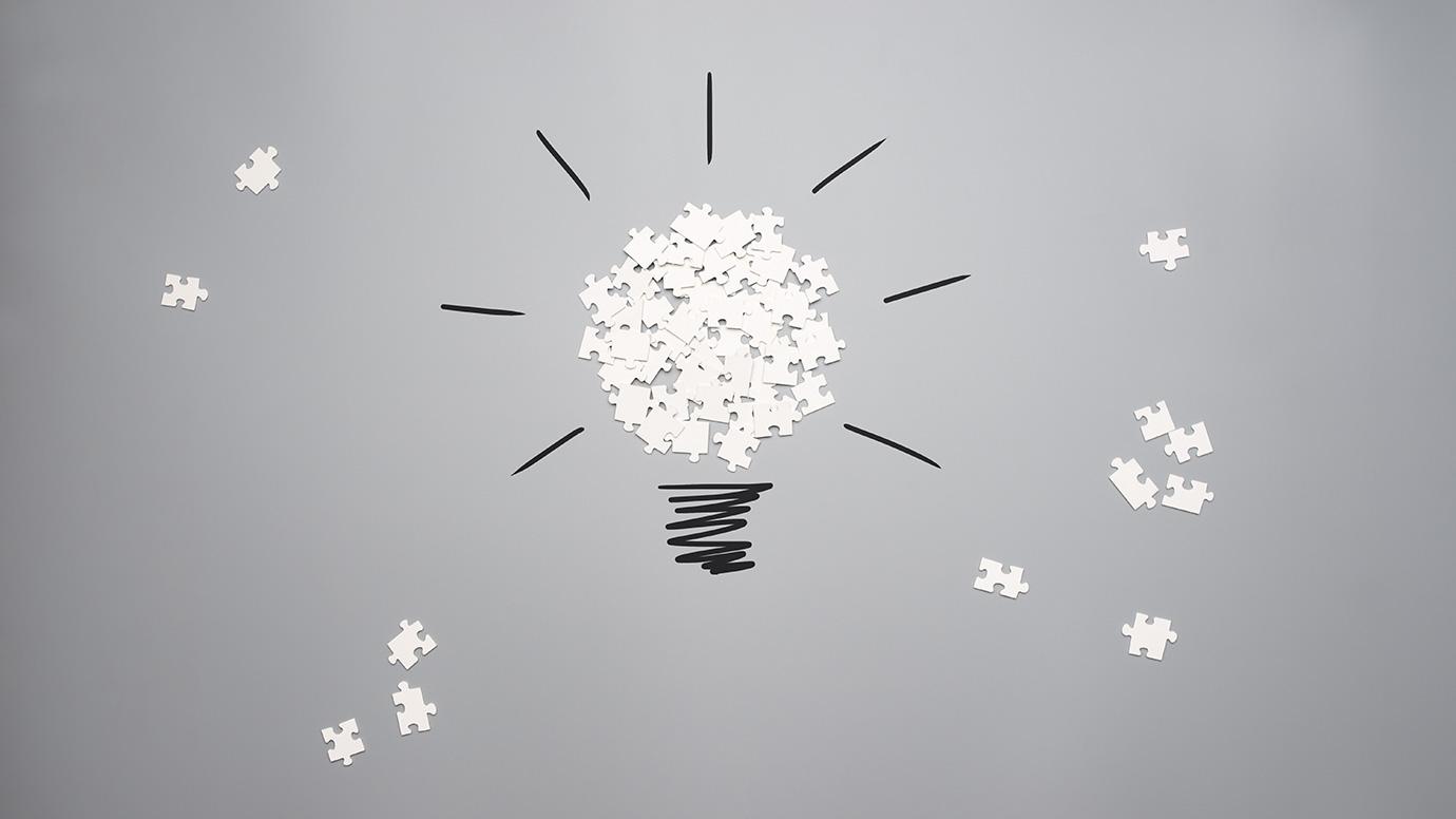 Scattered puzzle pieces forming a light bulb on a grey background