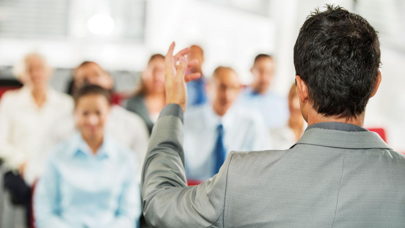 Male presenter giving a public speech in front of the business audience.